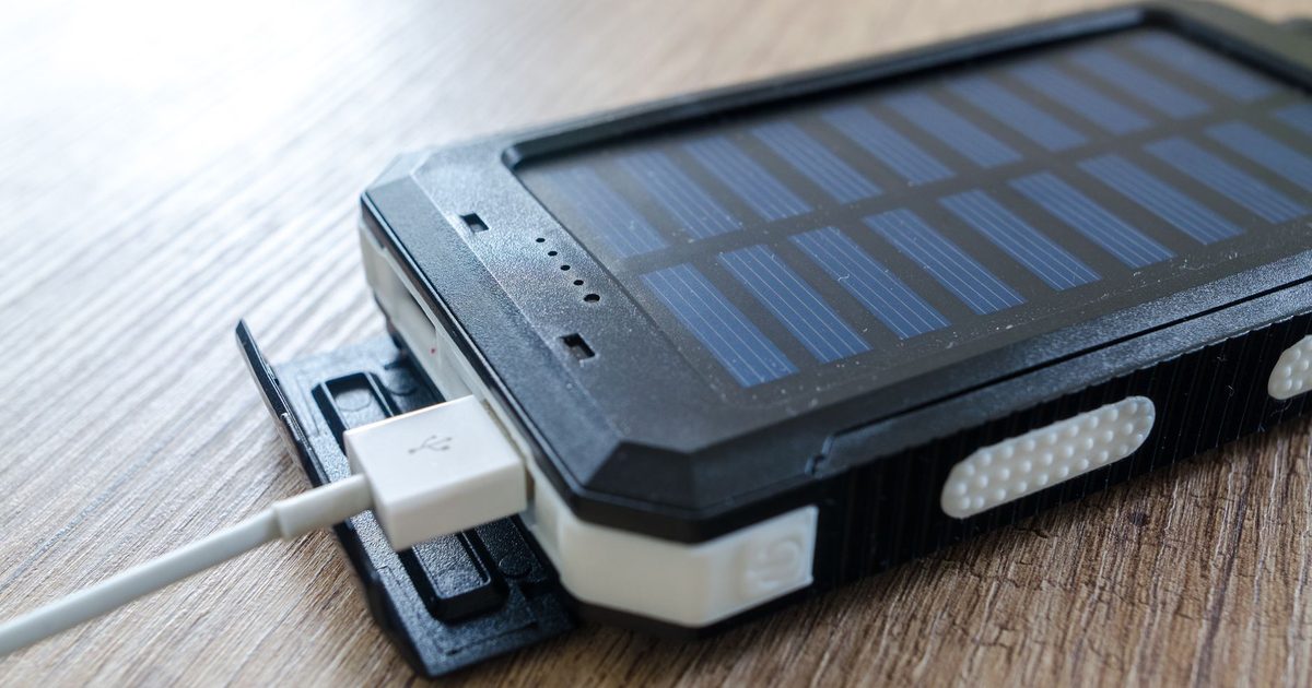 a rugged solar power bank on a desk with a charging cable plugged in