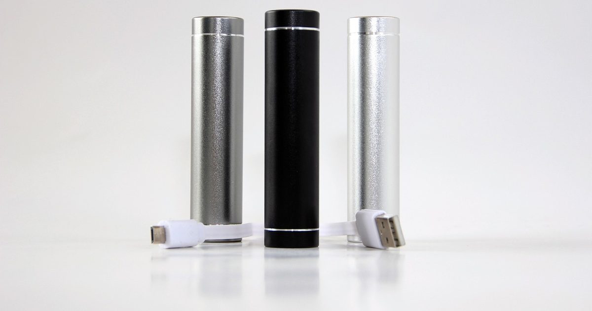 three cylindrical power banks standing upright with usb charging cables on white