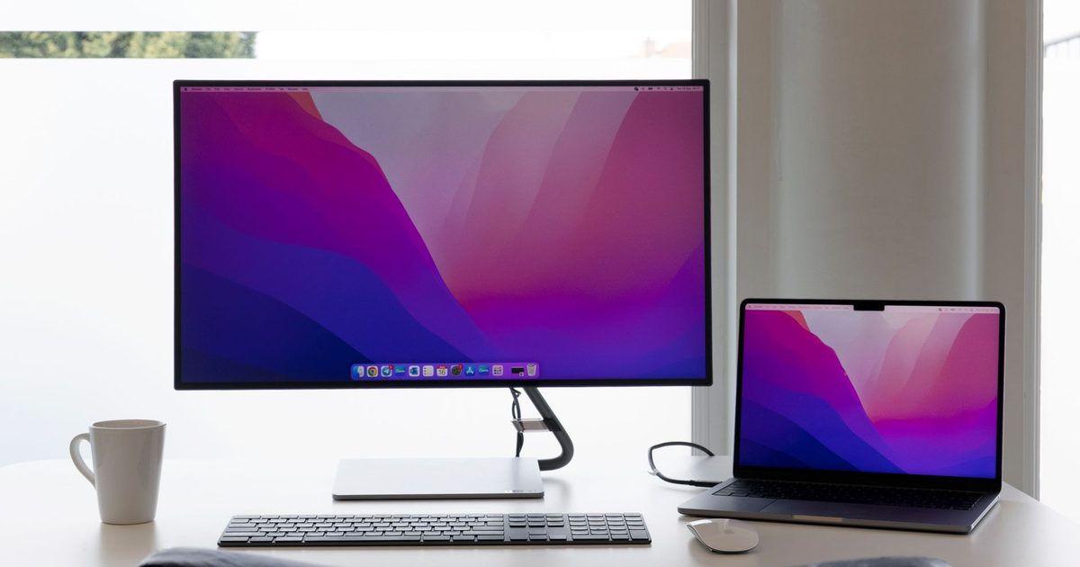 a laptop beside a large external monitor on a bright desk with a keyboard